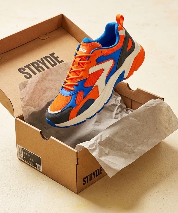 The STRYDE Runner 01 in orange, blue and cream, lifted out of its open box.